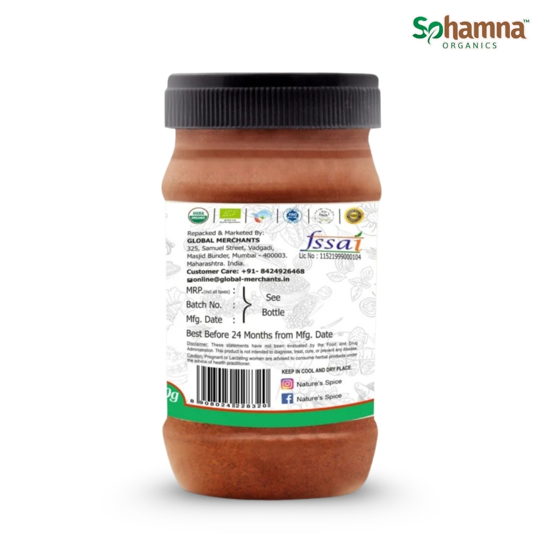 A 100g jar of Sohamna Organics BBQ Blend Powder shown from the back, featuring a black lid, brown contents, and a white label with green and blue text and logos, set against a plain white background.