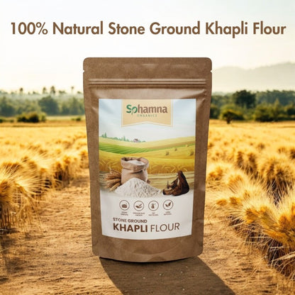 A stand-up pouch of Sohamna Organics Stone Ground Khapli Flour stands in the center of a golden wheat field. The packaging is brown with a white and green label.
