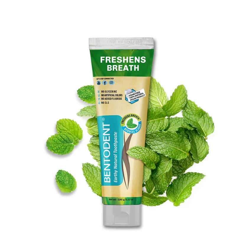 A tube of Bentodent Freshens Breath Lactate Natural Toothpaste is centered on a white background, surrounded by fresh green mint leaves. The tube is green and beige with blue accents.