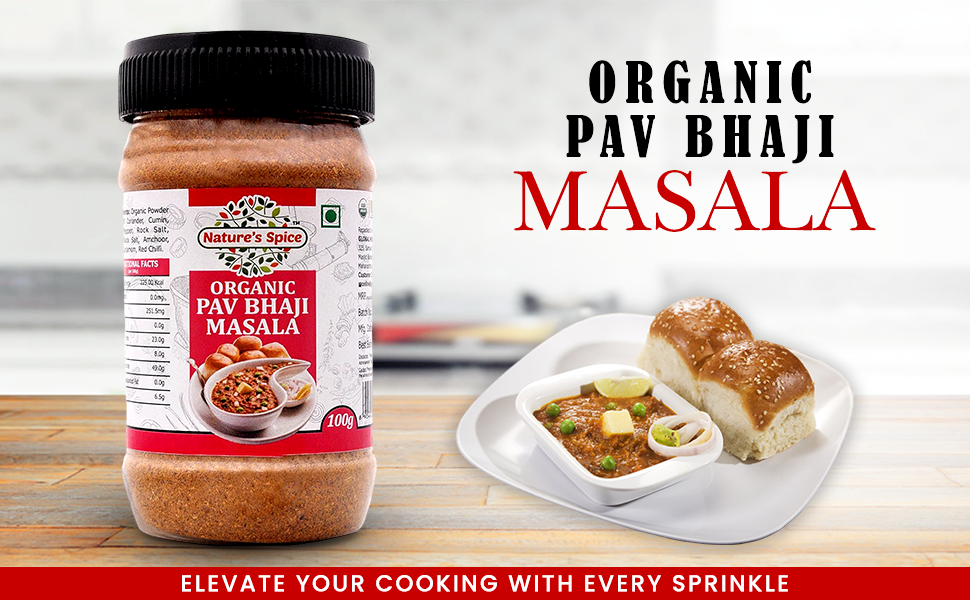 A jar of Sohamna Organics Pav Bhaji Masala displayed next to a plate of prepared Pav Bhaji with bread rolls and lime wedges, with text reading 'ORGANIC PAV BHAJI MASALA' on a bright, blurred kitchen background.