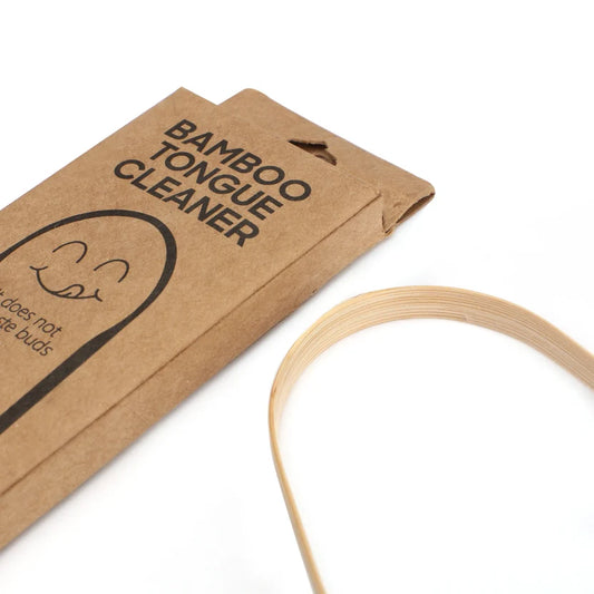 A bamboo tongue cleaner shown next to its brown kraft paper packaging on a clean white background.