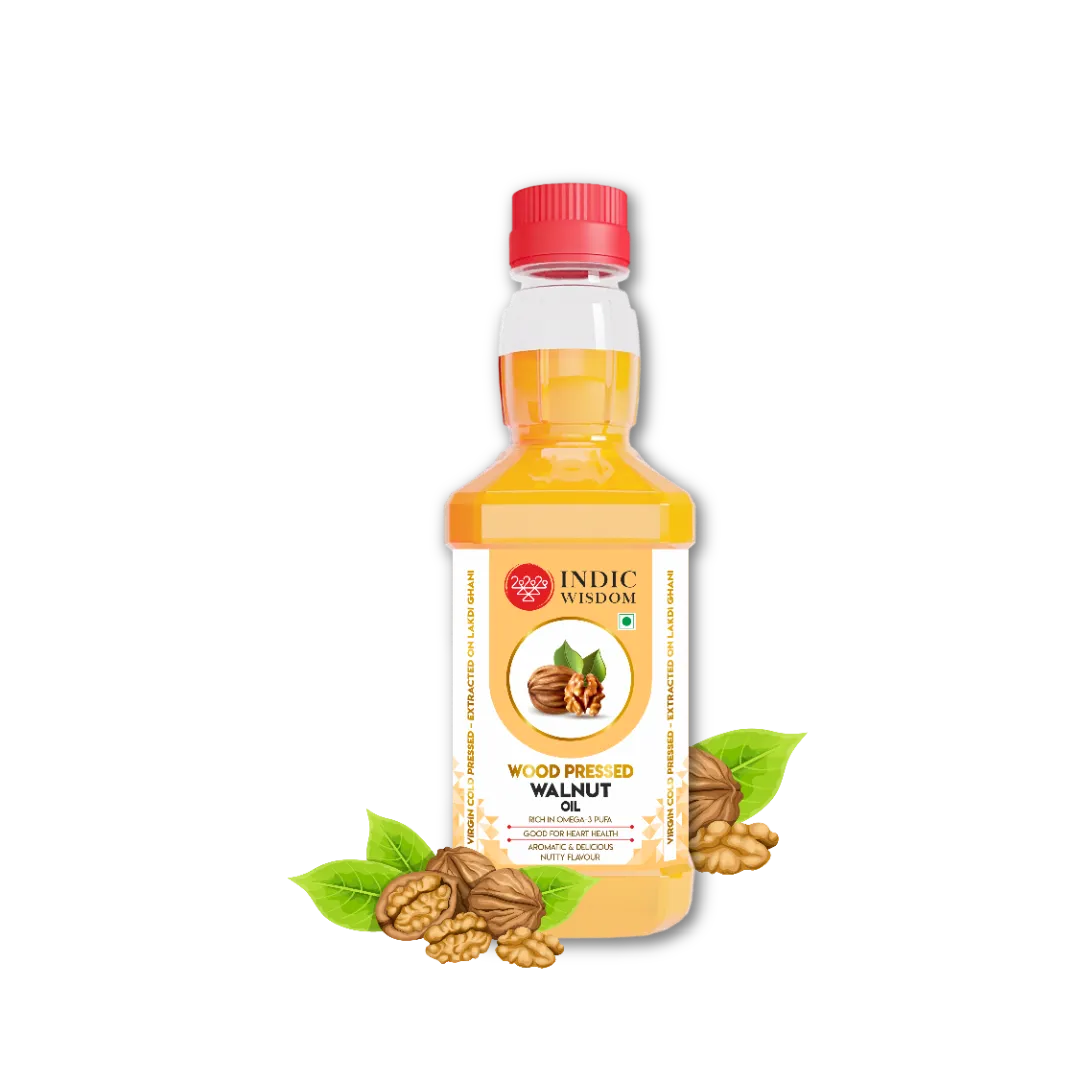 A bottle of Indic Wisdom Wood Preserved Walnut Oil with a red cap, shown on a white background with walnut shells and green leaves at the base of the bottle.