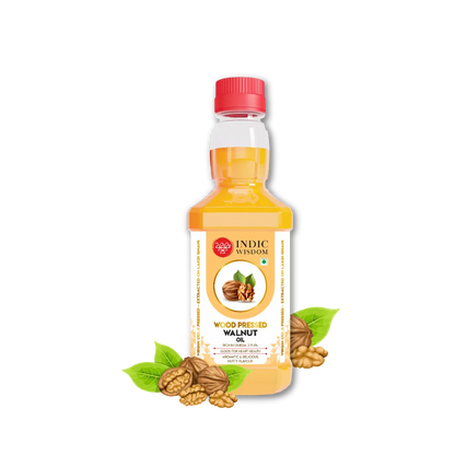 A bottle of Indic Wisdom Wood Preserved Walnut Oil with a red cap, shown on a white background with walnut shells and green leaves at the base of the bottle.